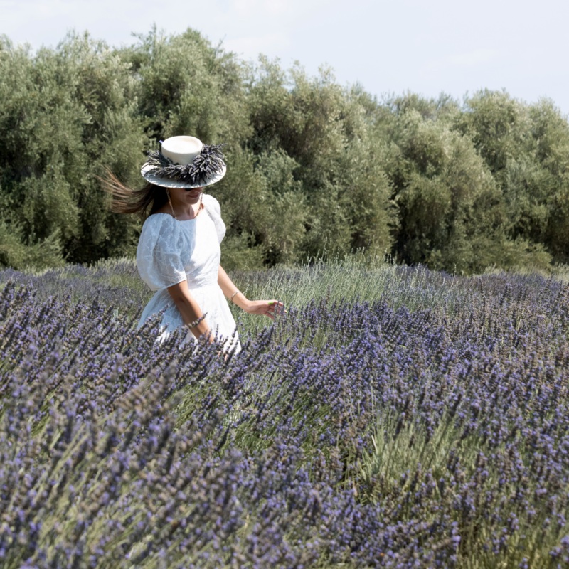 A woman in a lavender-trimmed hat walking through blooming lavender rows